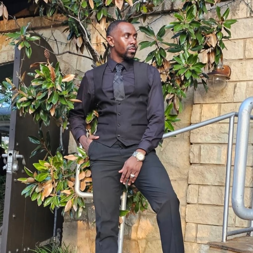 The Zarrelle advisor in a black vest and tie, standing on stone steps beneath a magnolia tree